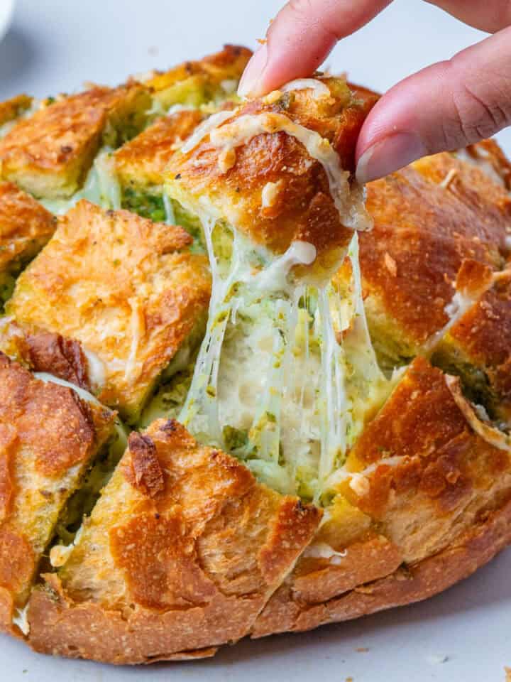 Cheesy pull apart bread with pesto with a piece being pulled out