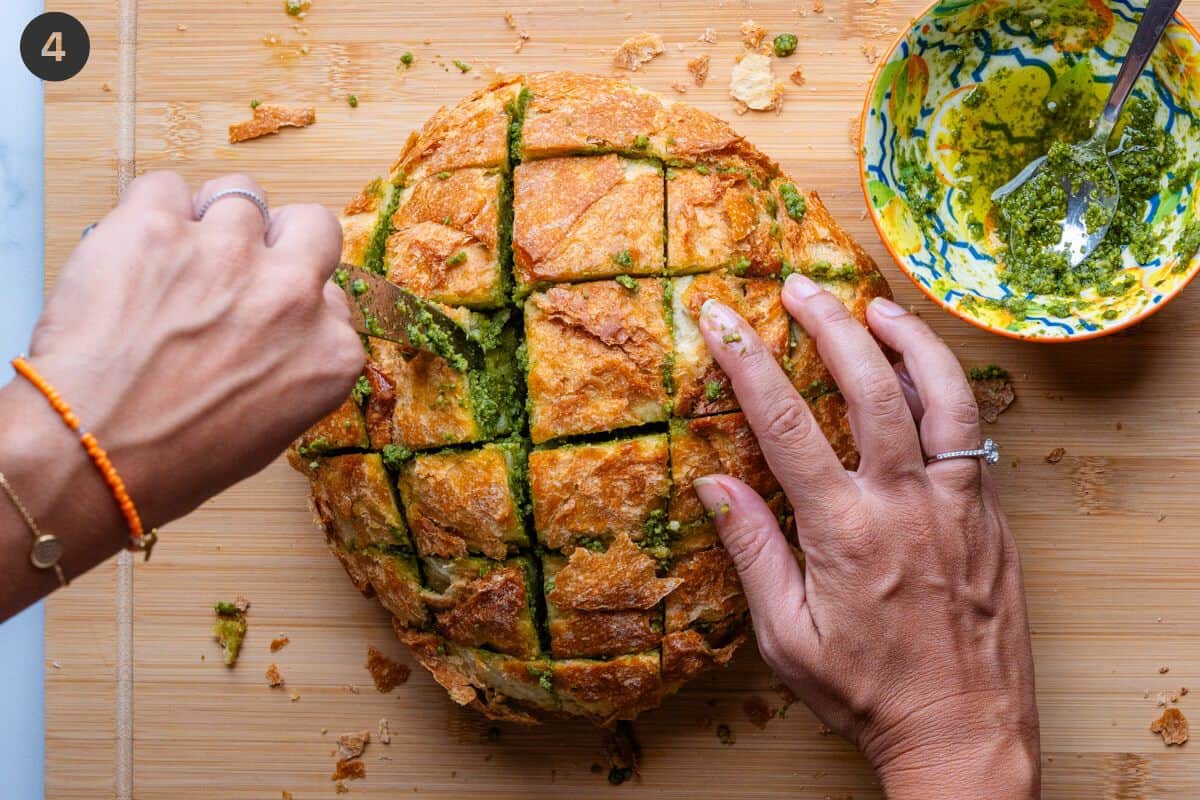 Pesto being placed into gaps in bread with a knife