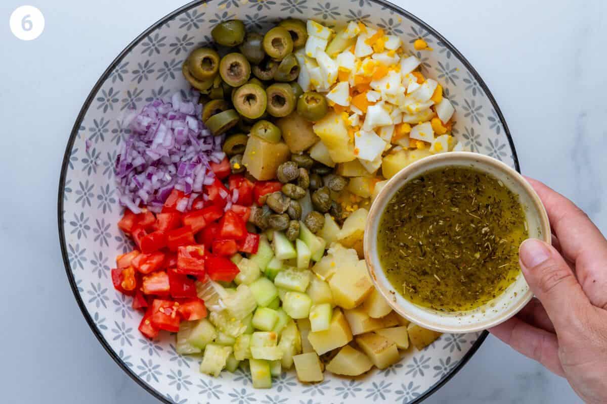 Dressing being poured into the a large bowl of ingredients