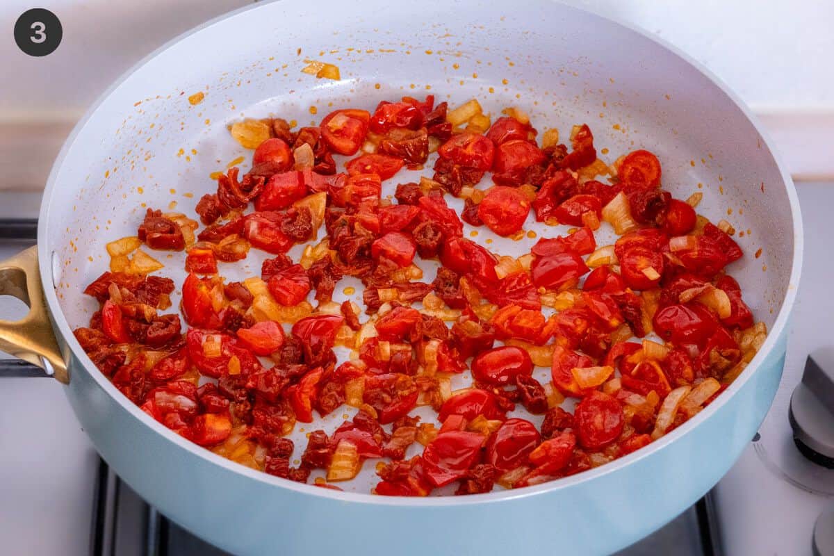 Sundried tomatoes, tomatoes and onions being sautéed in a pan