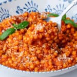 Spoon coming out of a bowl of fregola pasta with sugo