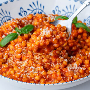 Spoon coming out of a bowl of fregola pasta with sugo