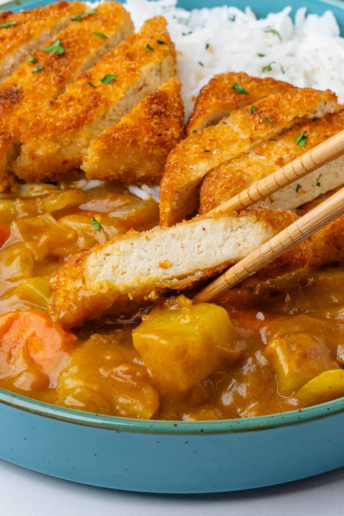 Focus on piece of tofu katsu with chopsticks in a bowl