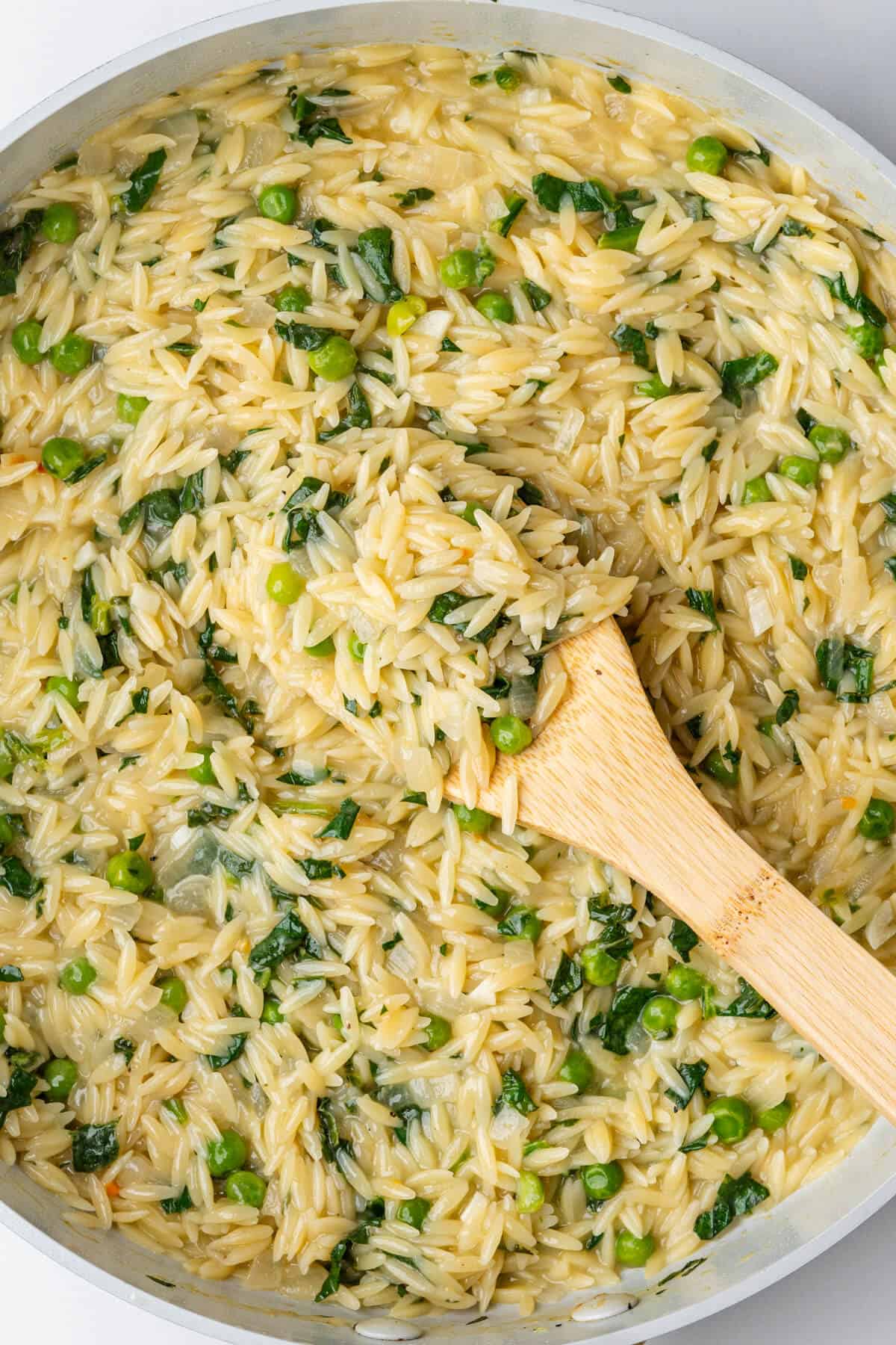 Wooden spoon in a large pan of lemon orzo pasta