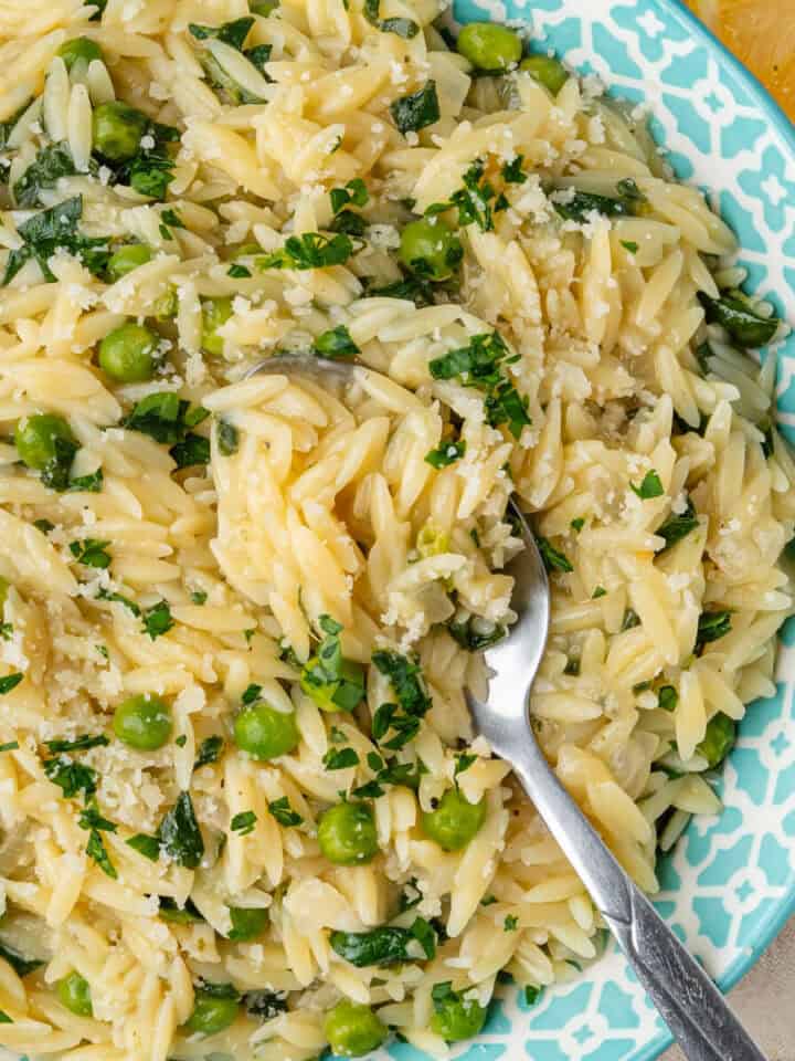 Spoon in a bowl of lemon orzo with peas and spinach