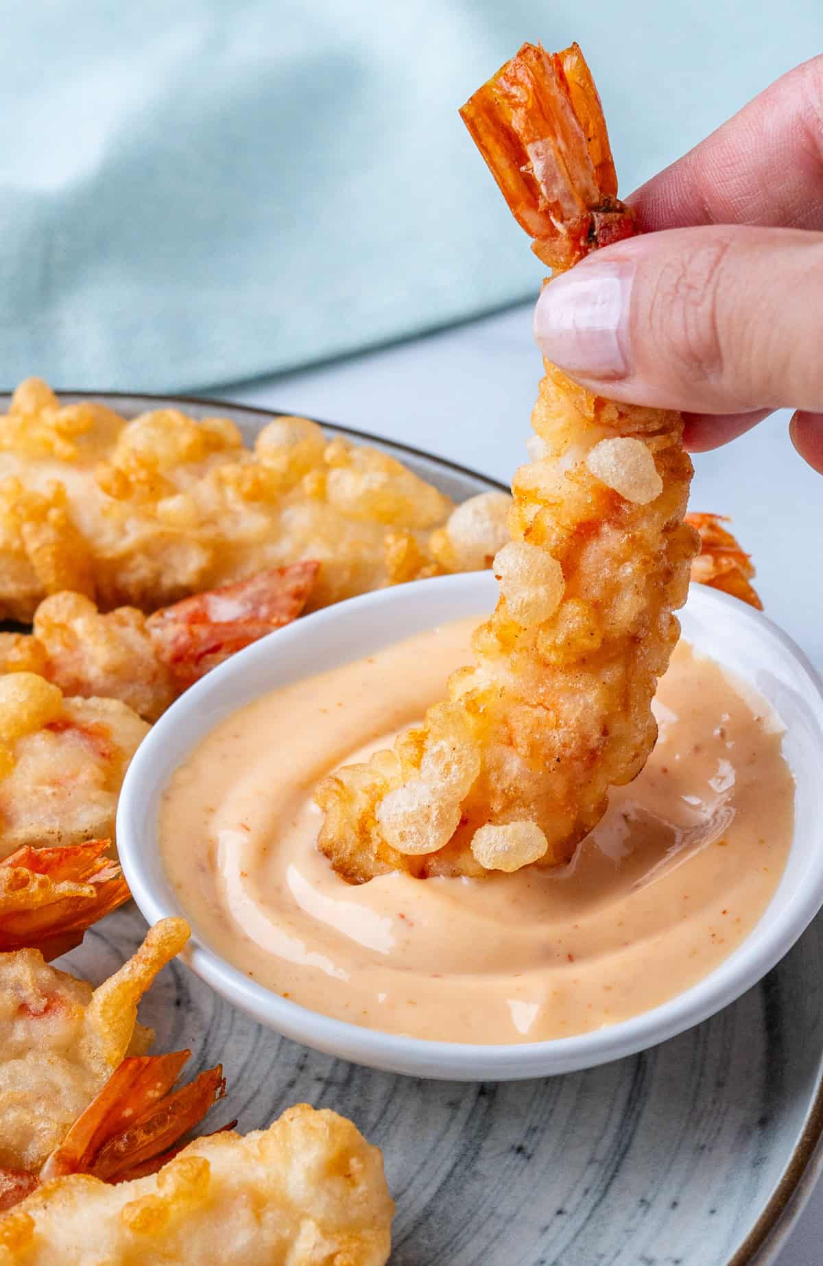 Piece of shrimp tempura being dipped into sriracha aioli