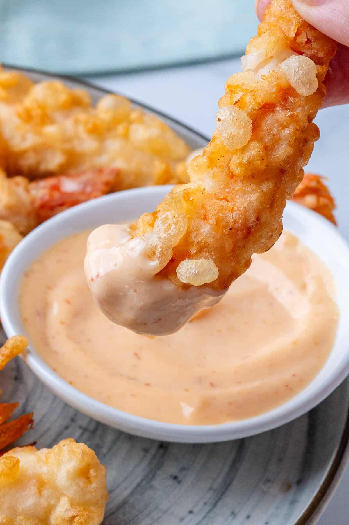 Piece of tempura just dipped into sriracha aioli