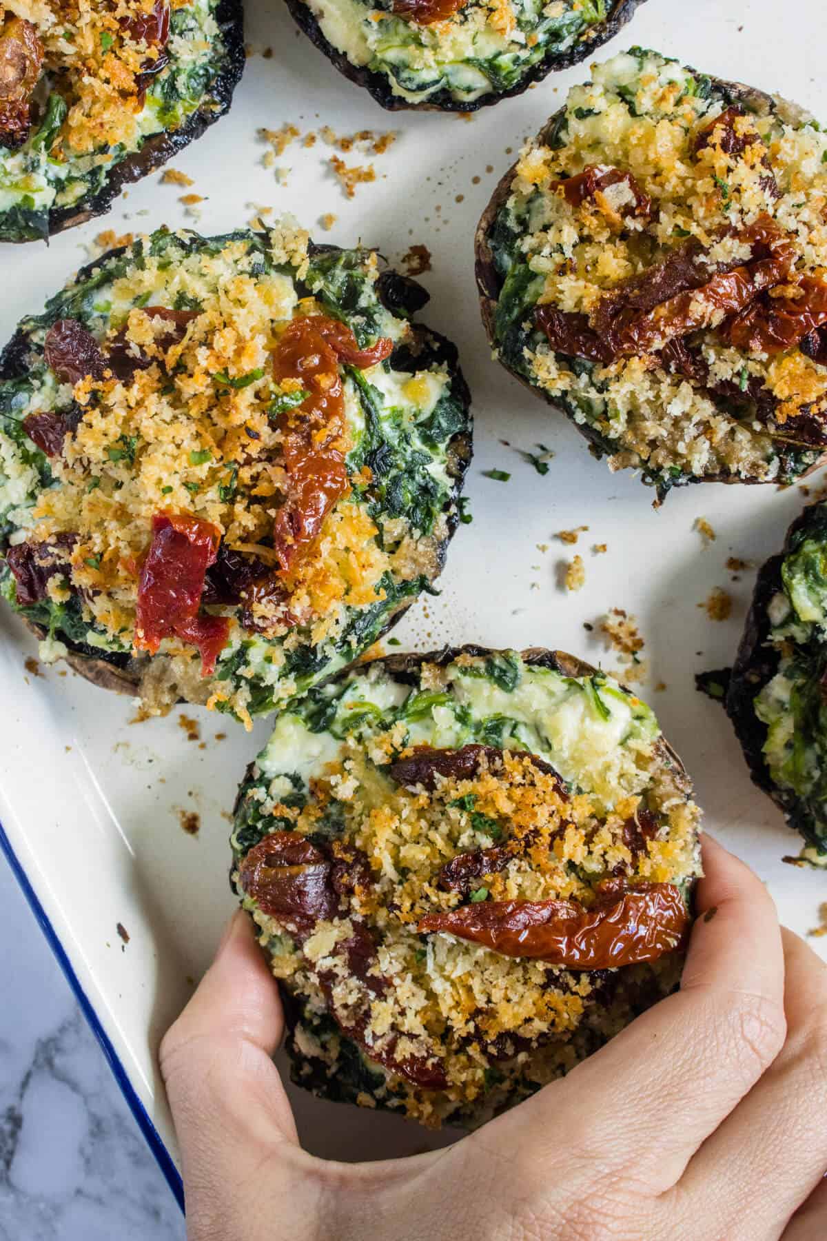 Hand picking up a stuffed portobello mushrooms from an oven tray of mushrooms