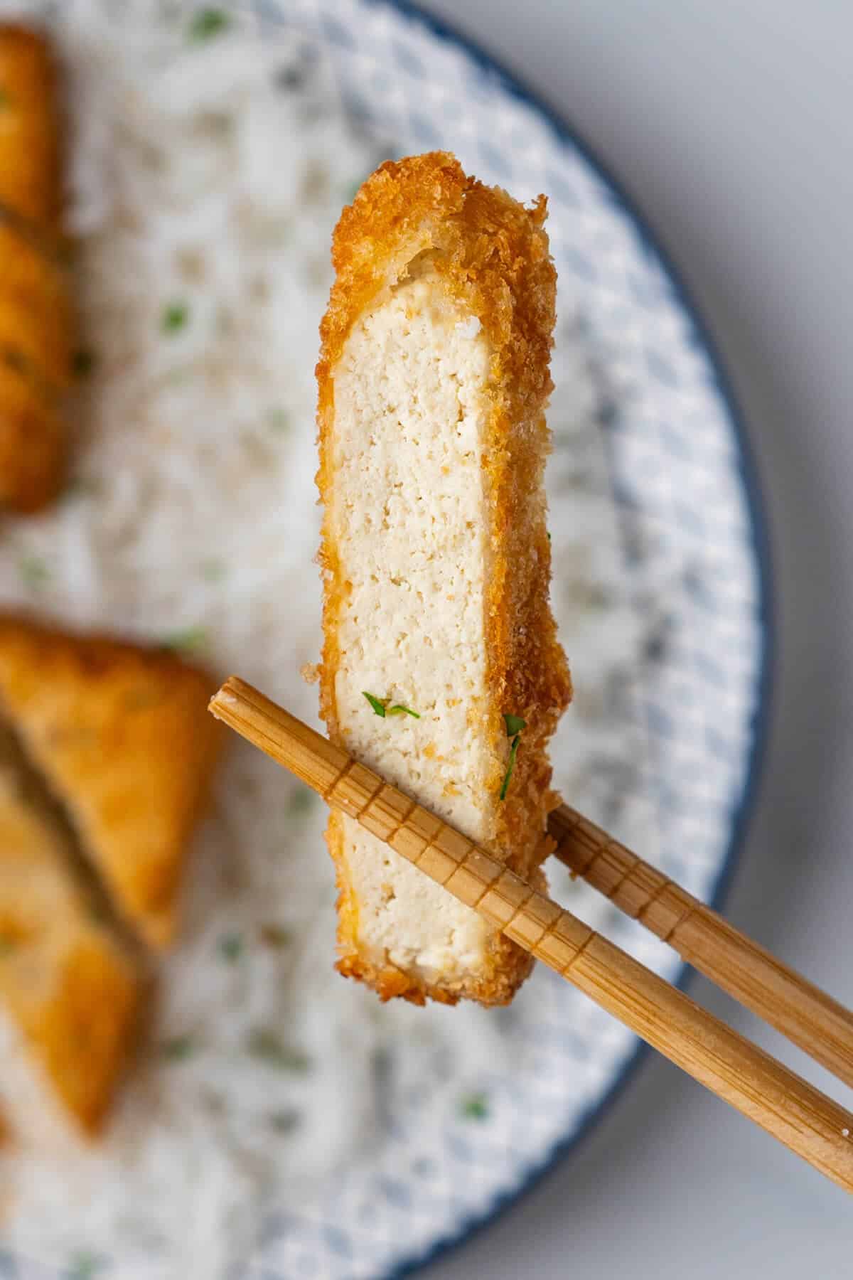 Close up of a piece of tofu held with chopsticks