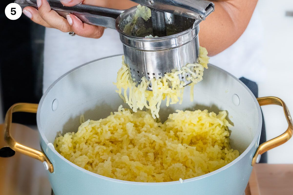 Cooked potatoes being mashed with a masher