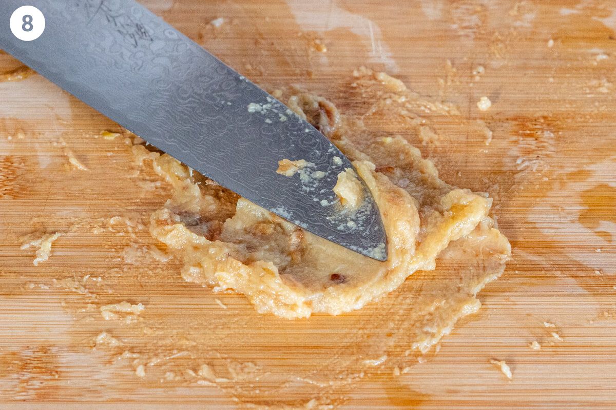 Knife mashing the garlic to make a paste