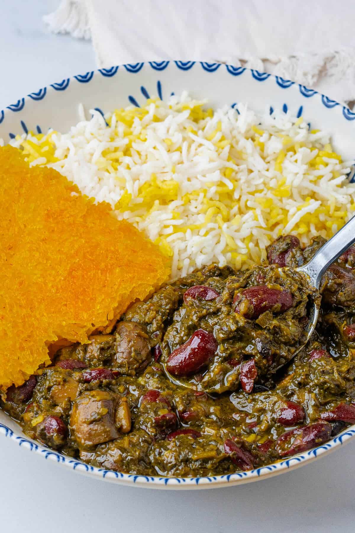 Spoon coming out of the bowl of Ghormeh Sabzi with rice and saffron tahdig