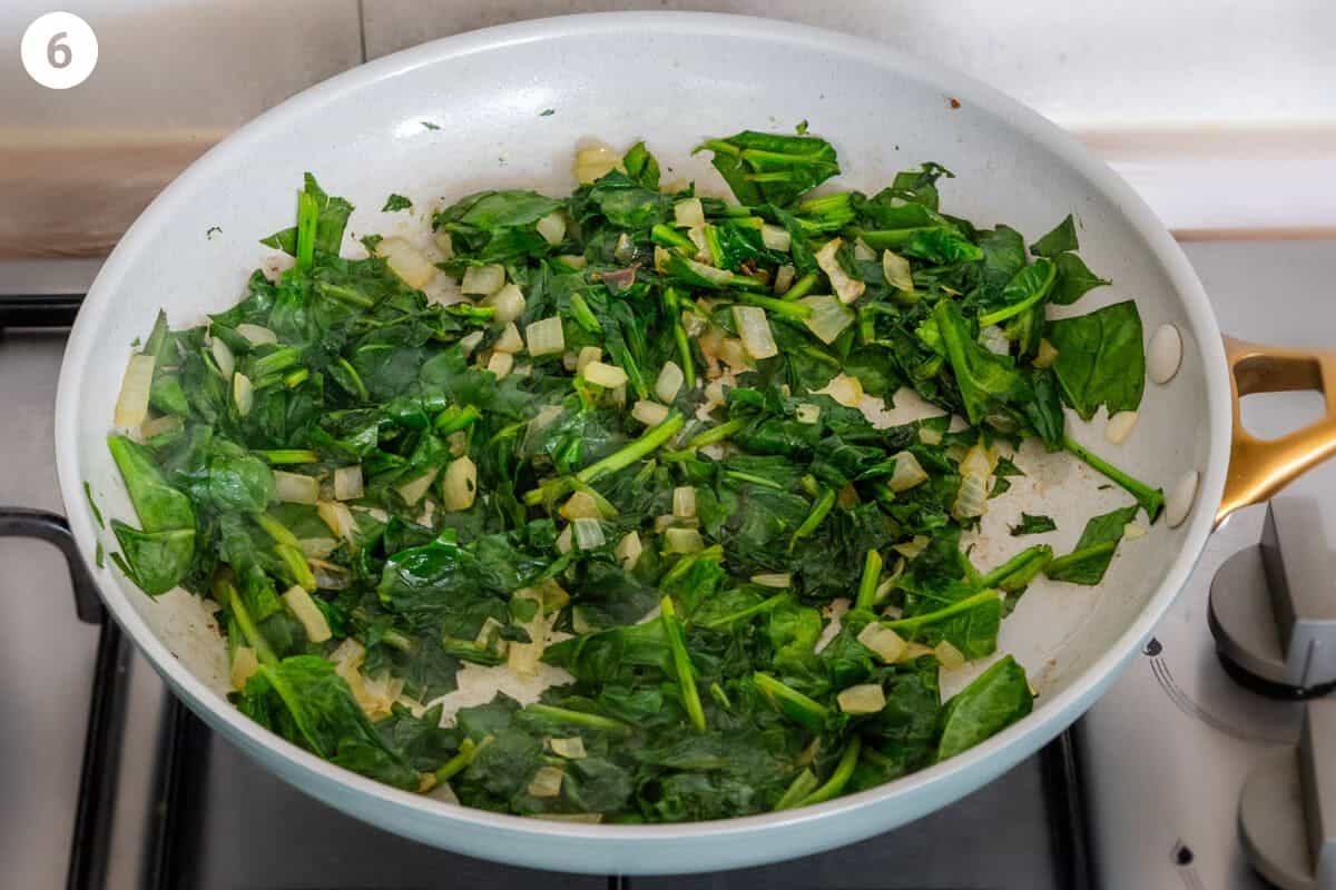 Spinach being sautéed with onion in a pan