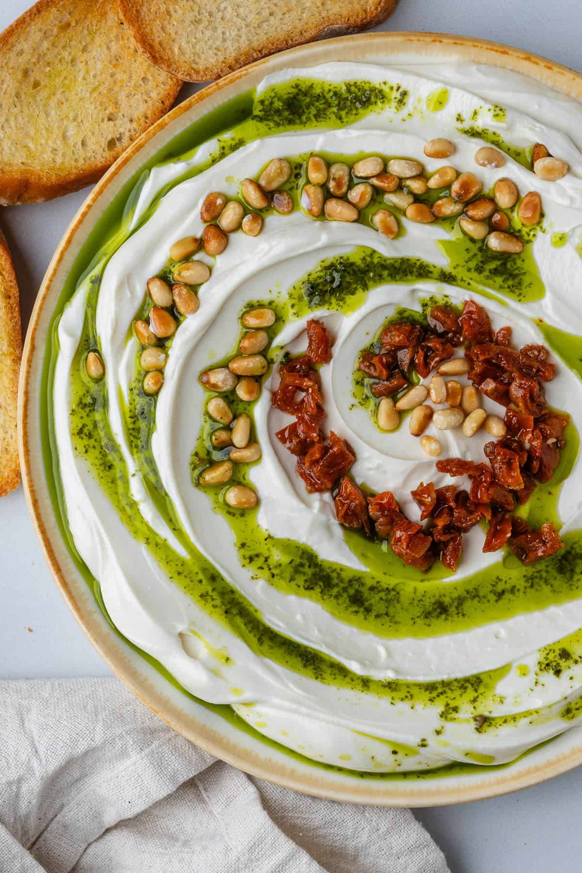 Ricotta in a bowl topped with basil oil, pine nuts and sun dried tomatoes