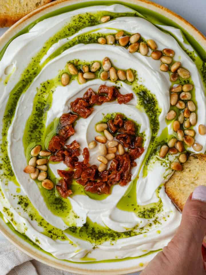 Bread dipping into whipped ricotta with basil oil, pine nuts and sun dried tomatoes