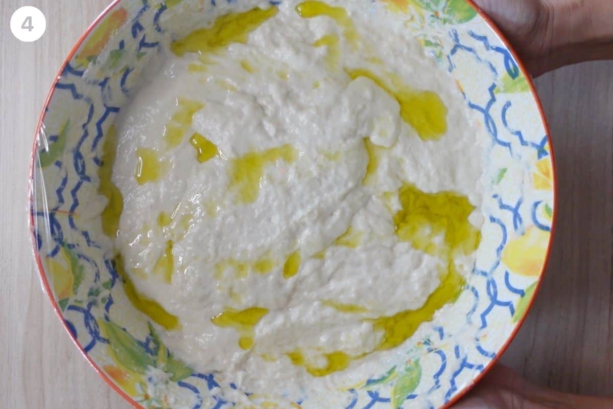 Dough topped with olive oil and covered with cling wrap