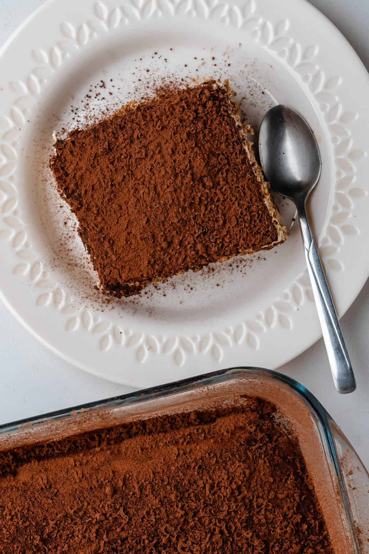 Tiramisu on a plate with a spoon and tray on the side