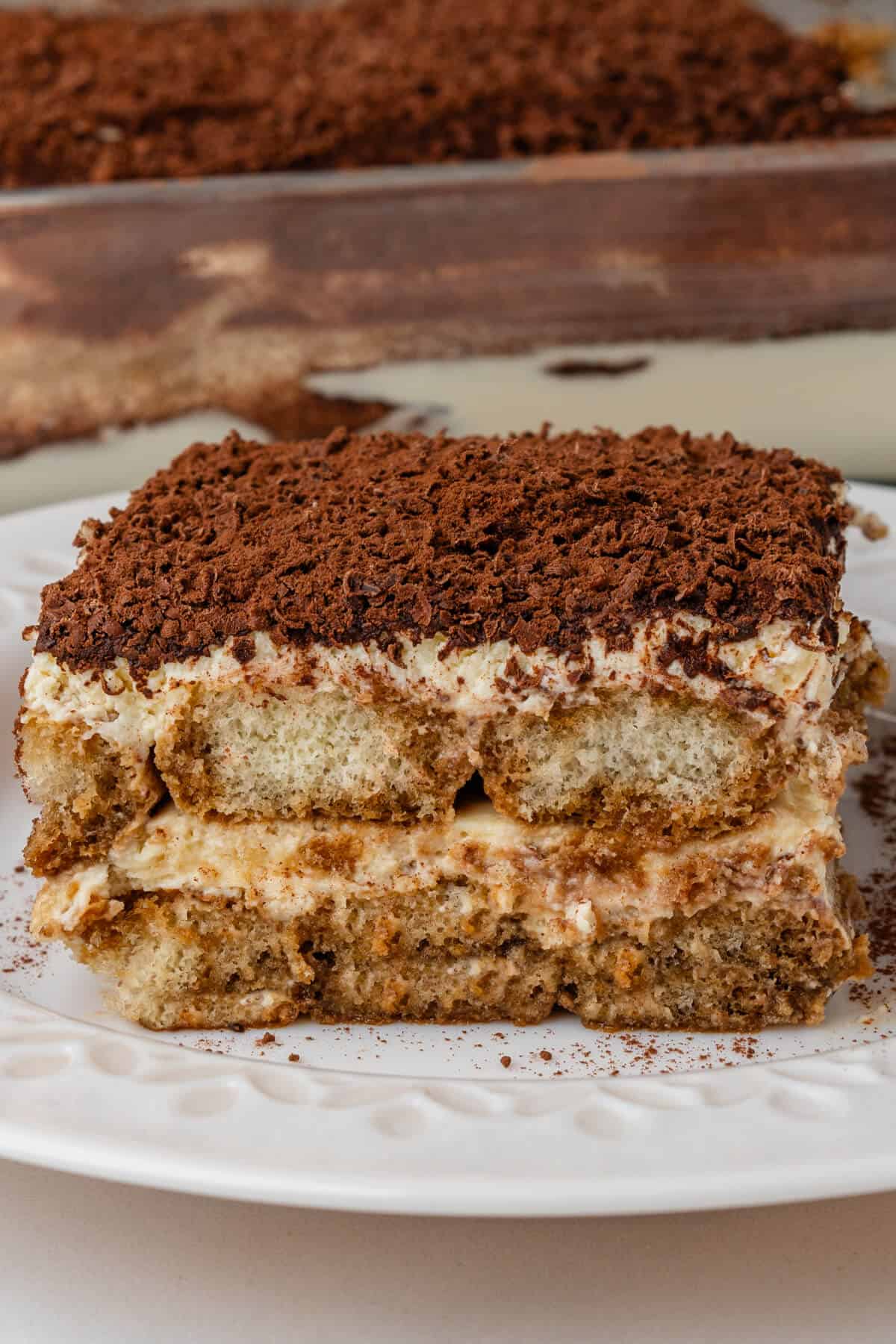 Piece of tiramisu on a plate with tray in the background