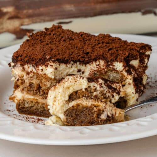 Piece of tiramisu on a plate with a spoonfull