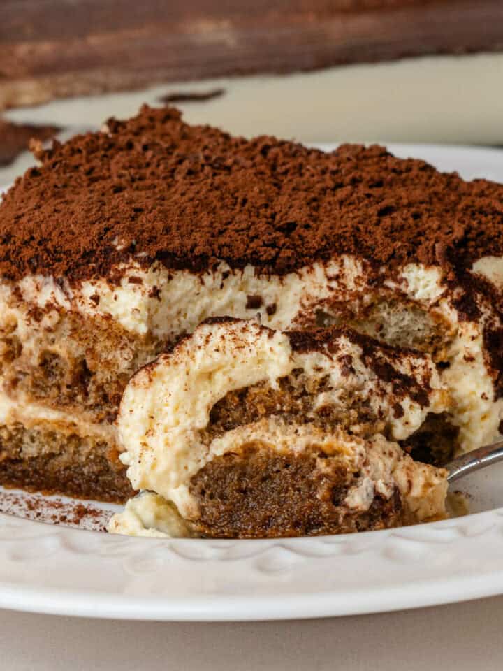 Piece of tiramisu on a plate with a spoonfull