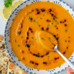 Spoon in a bowl of Turkish lentil soup (Mercimek Çorbası) and Aleppo pepper oil