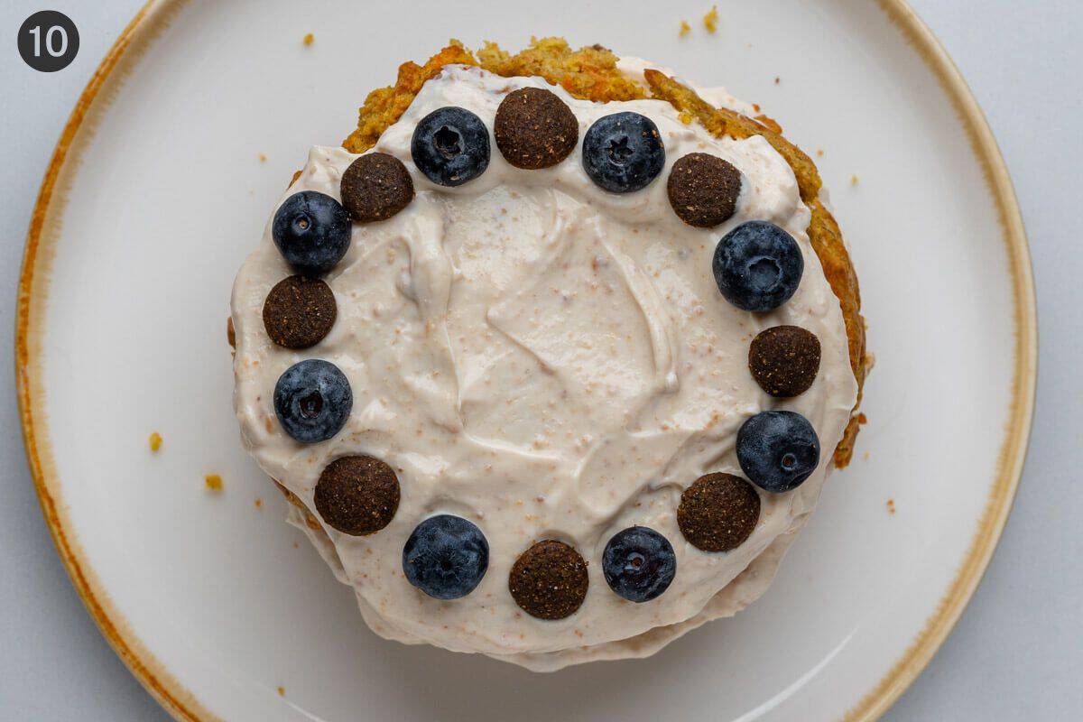 Top cake layer added with frosting and garnish of blueberries and dog treats