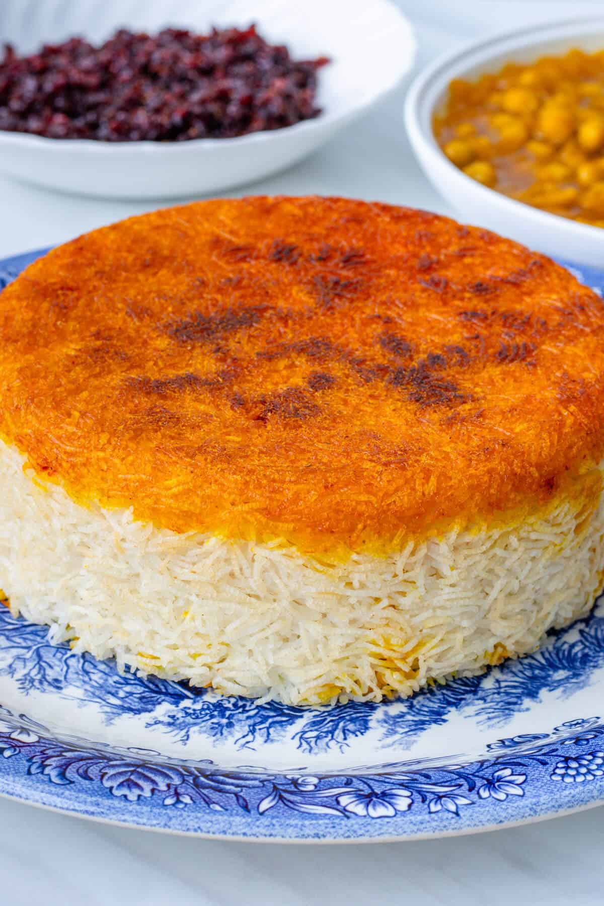 Saffron tahdig rice on a plate with chickpea stew and barberries on the side