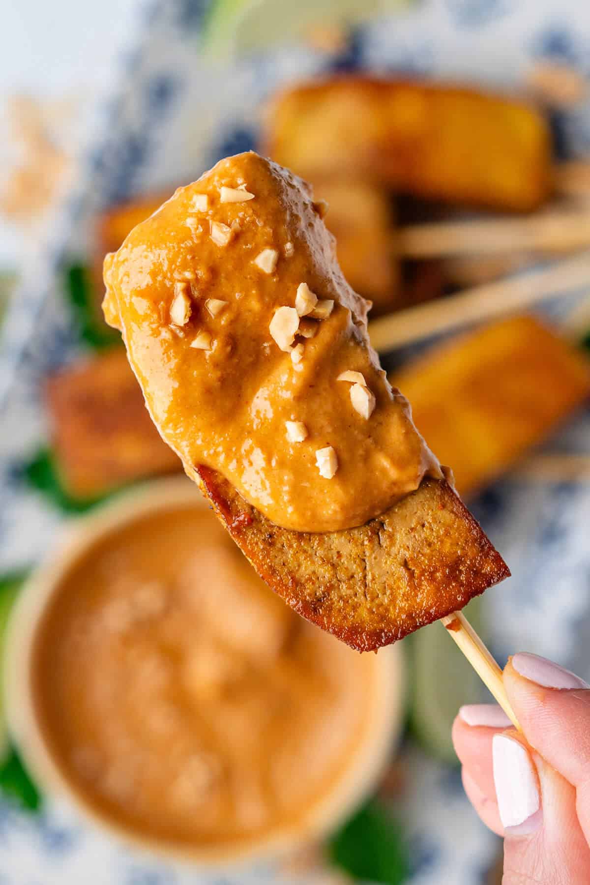 Close up of piece of tofu satay dipped into sauce