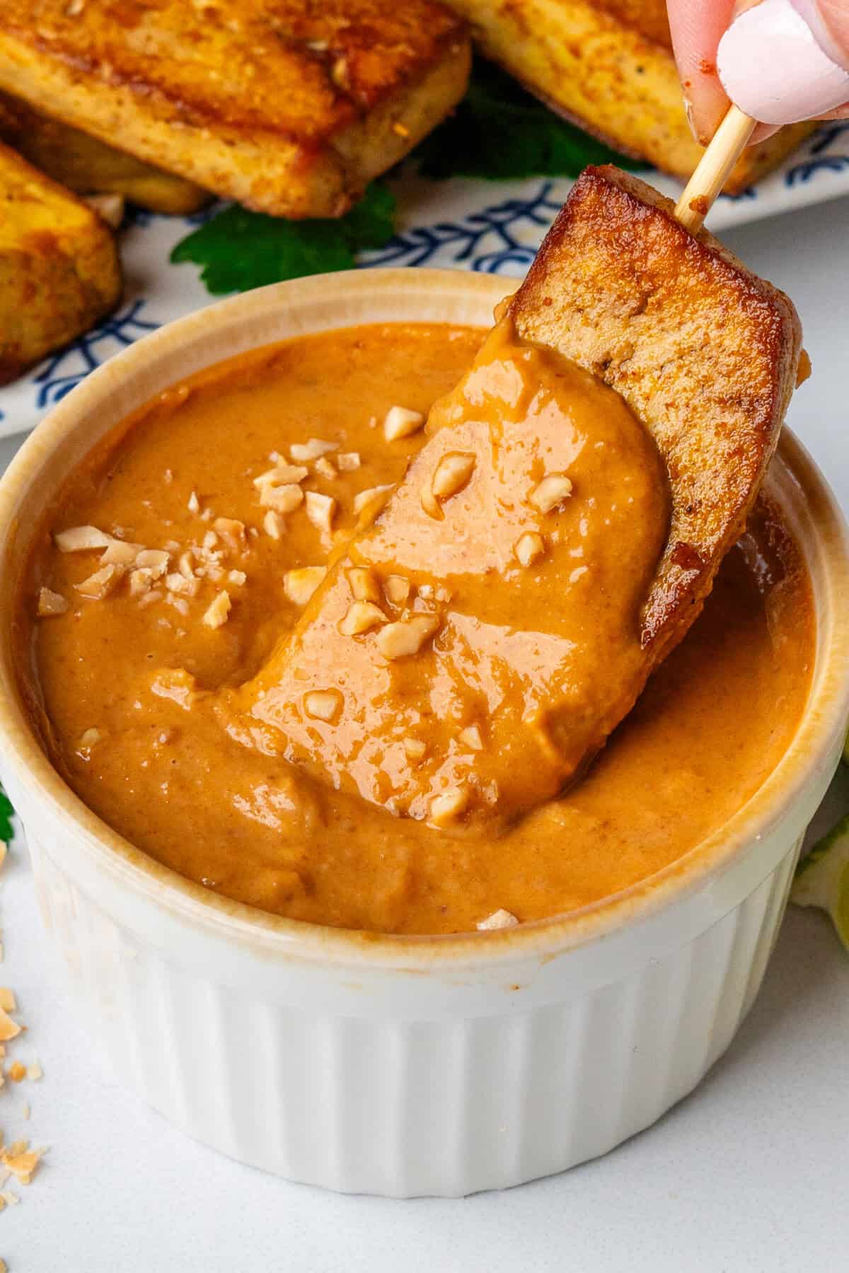 Tofu being dipped into satay sauce