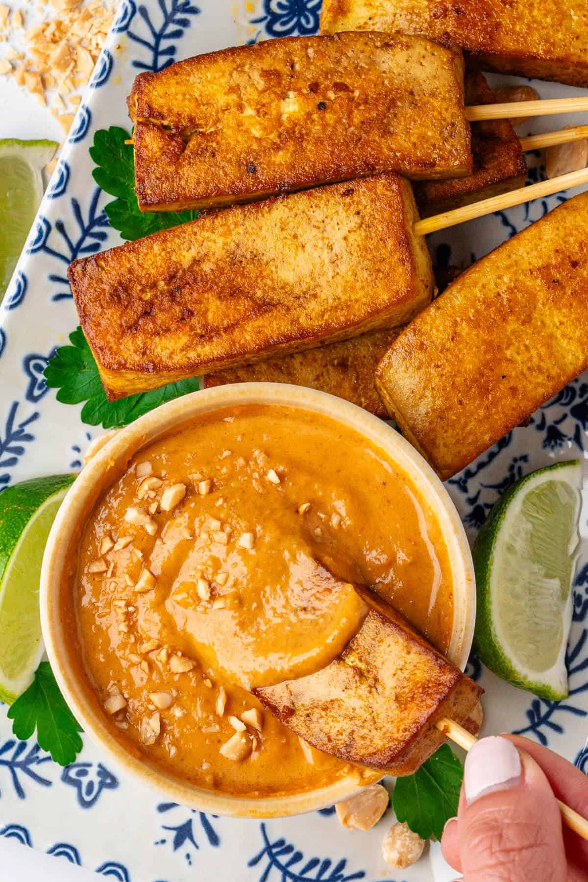 Piece of tofu satay being dipped into satay sauce