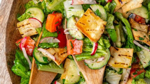Fattoush salad in a large bowl with wooden spoons
