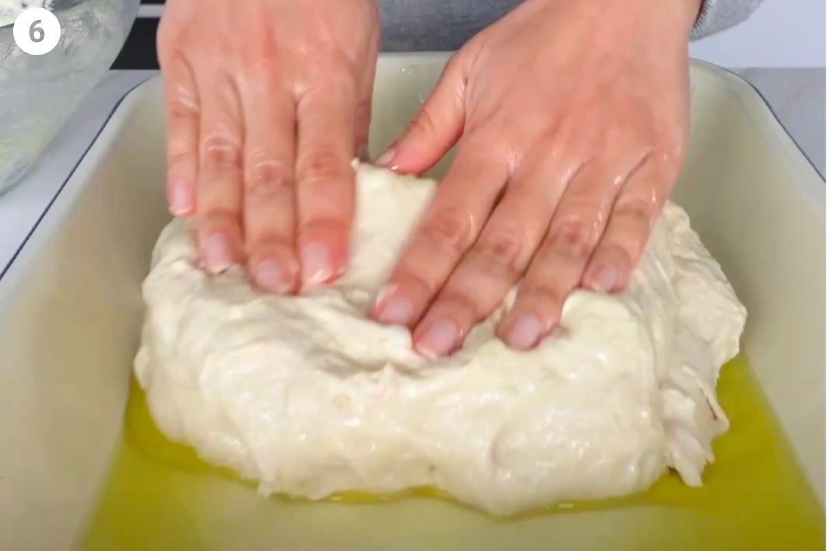 Dough added to oiled pan and being stretched out with hands