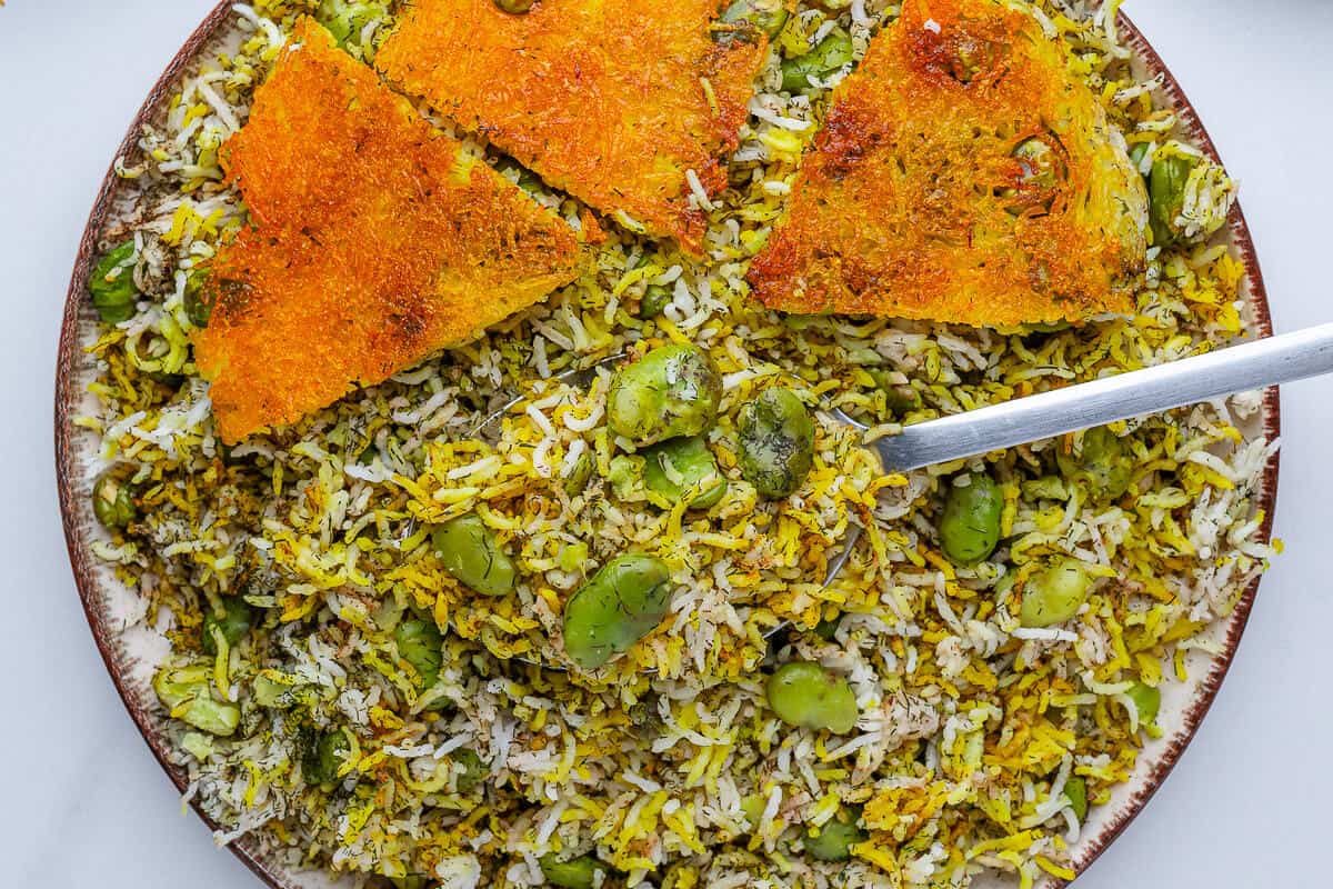 Plate of Baghali Polo with a spoon and pieces of tahdig on the side