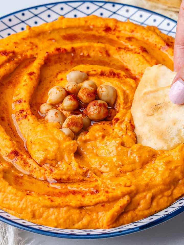 Roasted red pepper hummus with pita chip being dipped in