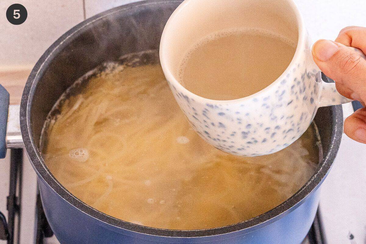 A mug taking some pasta water out of the pot