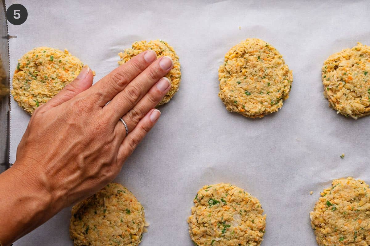 Fingers gently pressing down on the fritters to flatten them