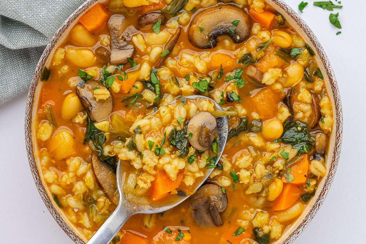 Spoon in a bowl of barley soup packed with vegetables