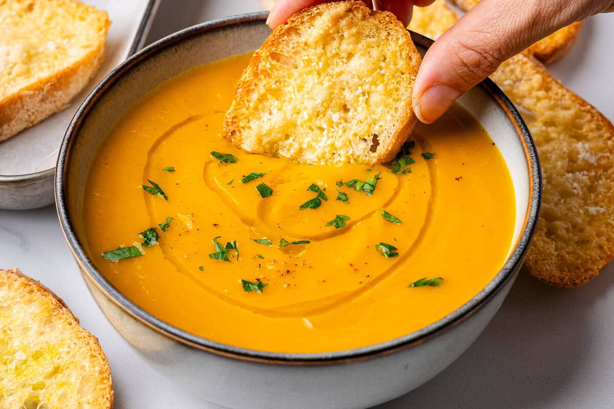 Crostini bread being dipped into a bowl of carrot soup
