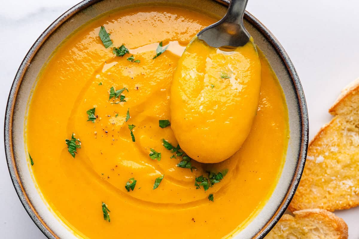 Spoon coming out of a bowl of carrot soup