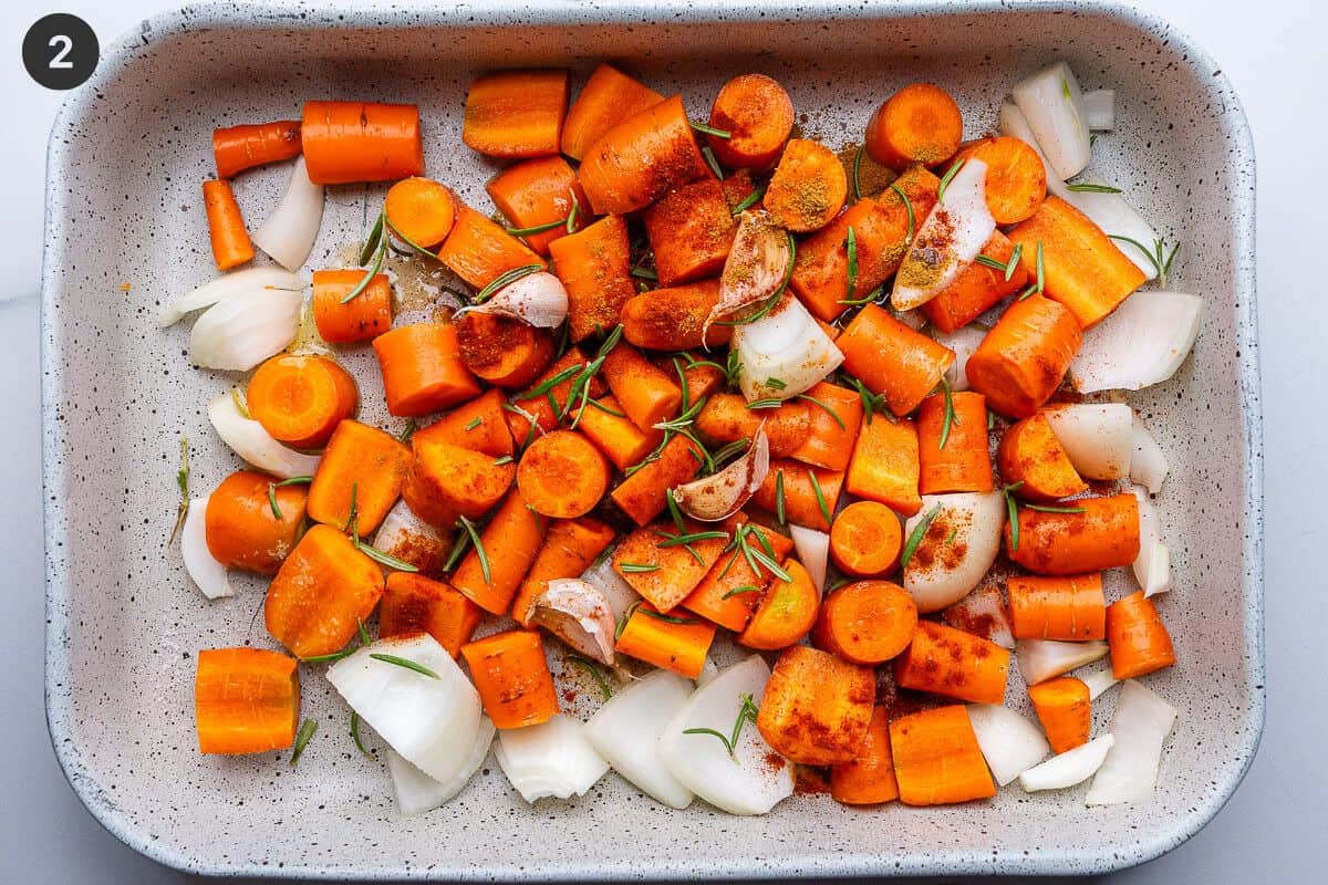 Carrots, onion and garlic added to a baking dish with spices and rosemary