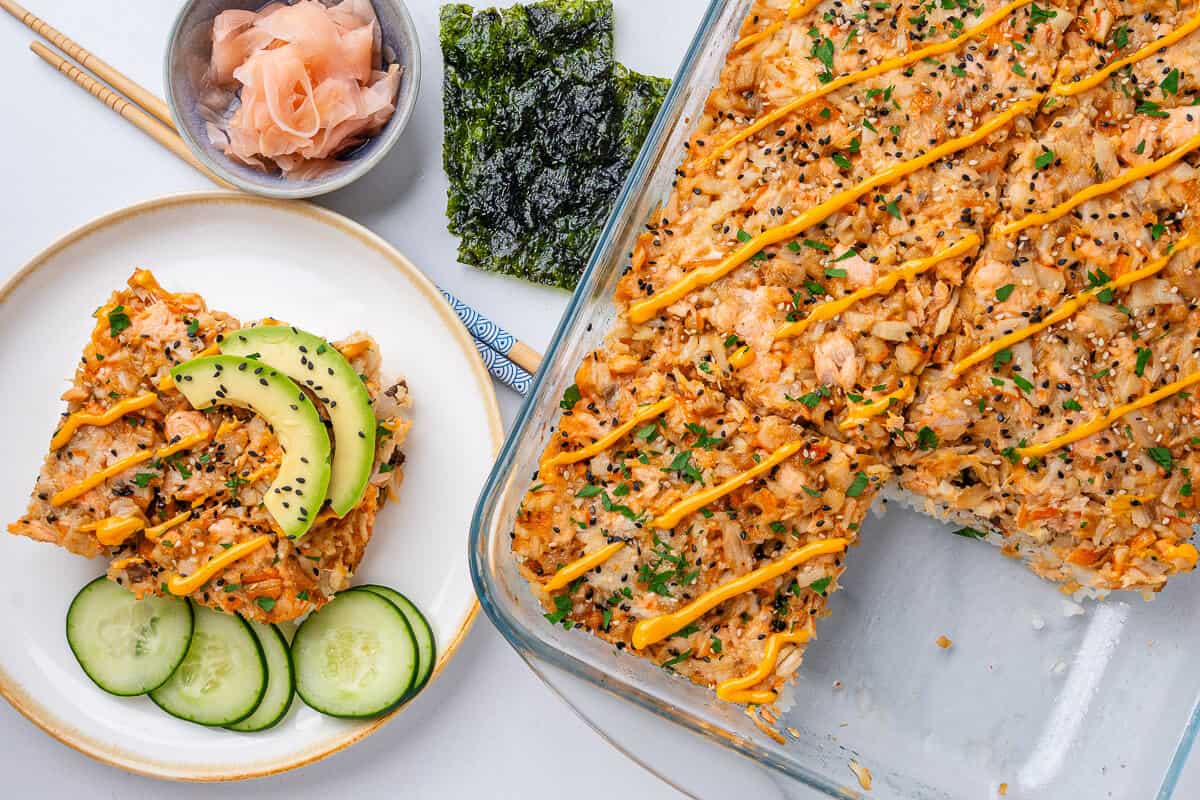 Sushi bake tray with a piece served on a plate with avocado, cucumber and spicy mayo