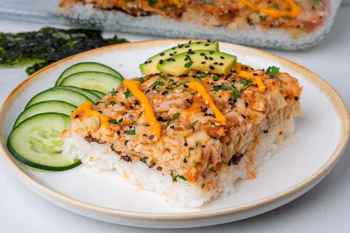 Piece of sushi bake on a plate with cucumber, avocado and spicy mayo