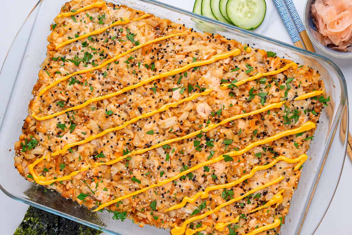 Tray of sushi topped with spicy mayo, with cucumbers and fresh ginger on the side