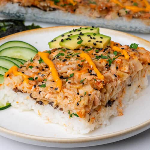 Piece of sushi bake on a plate topped with avocado, spicy mayo and sesame seeds