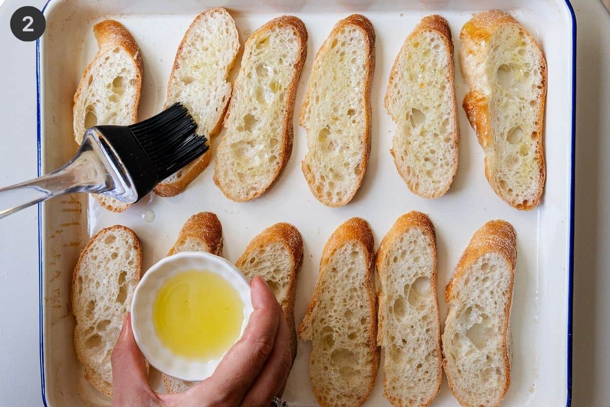 Olive oil being brushed on bread pieces on an oven tray