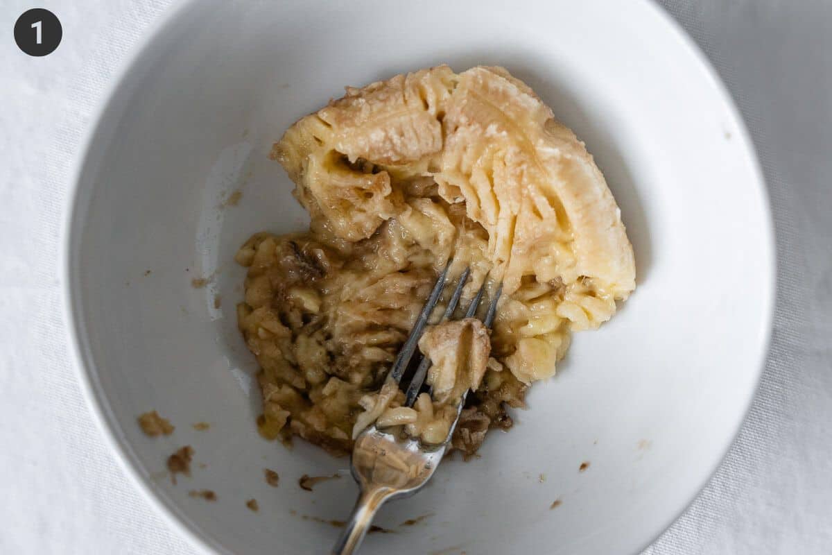 Banana being mashed with a fork in a bowl