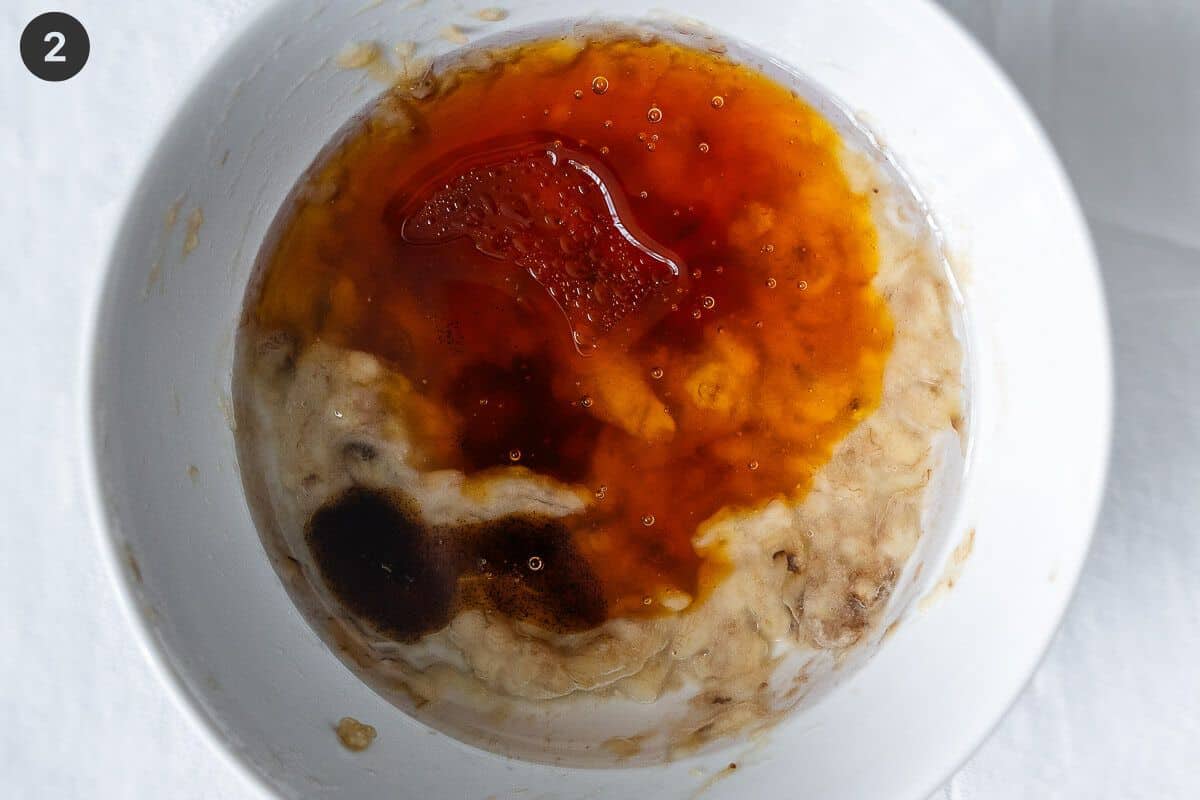 Wet ingredients added to mashed banana in a bowl