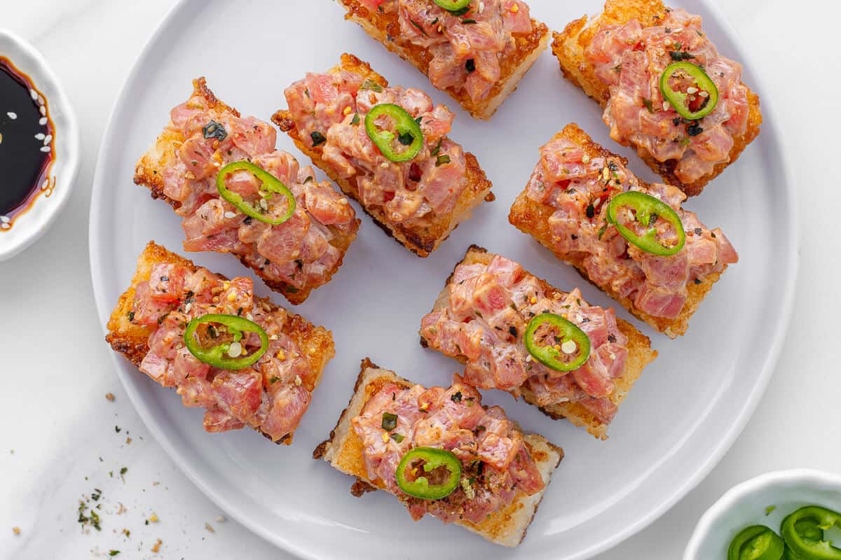 Plate of spicy tuna crispy rice pieces with dipping sauce and jalapeños on the side