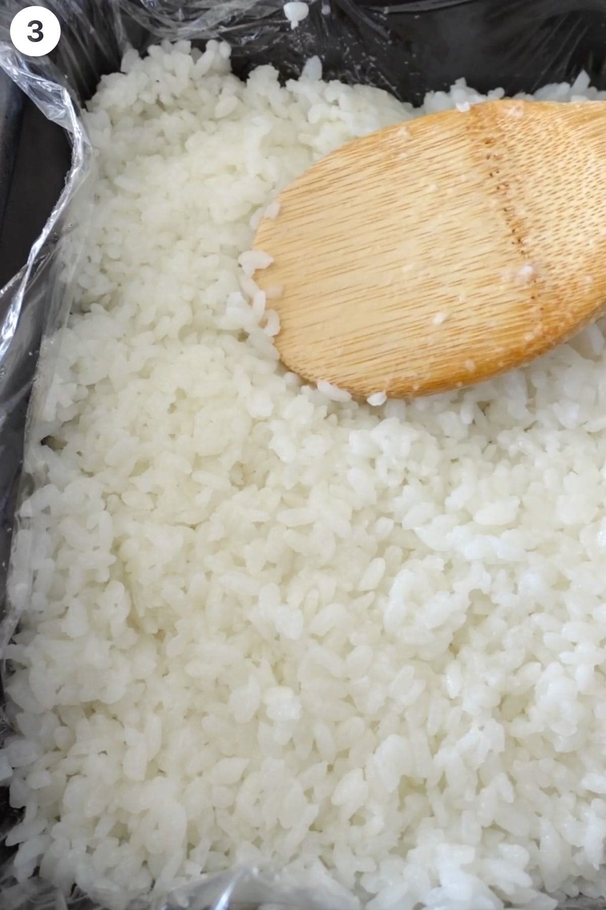 Cooked rice being flatten in a dish with a wooden spoon