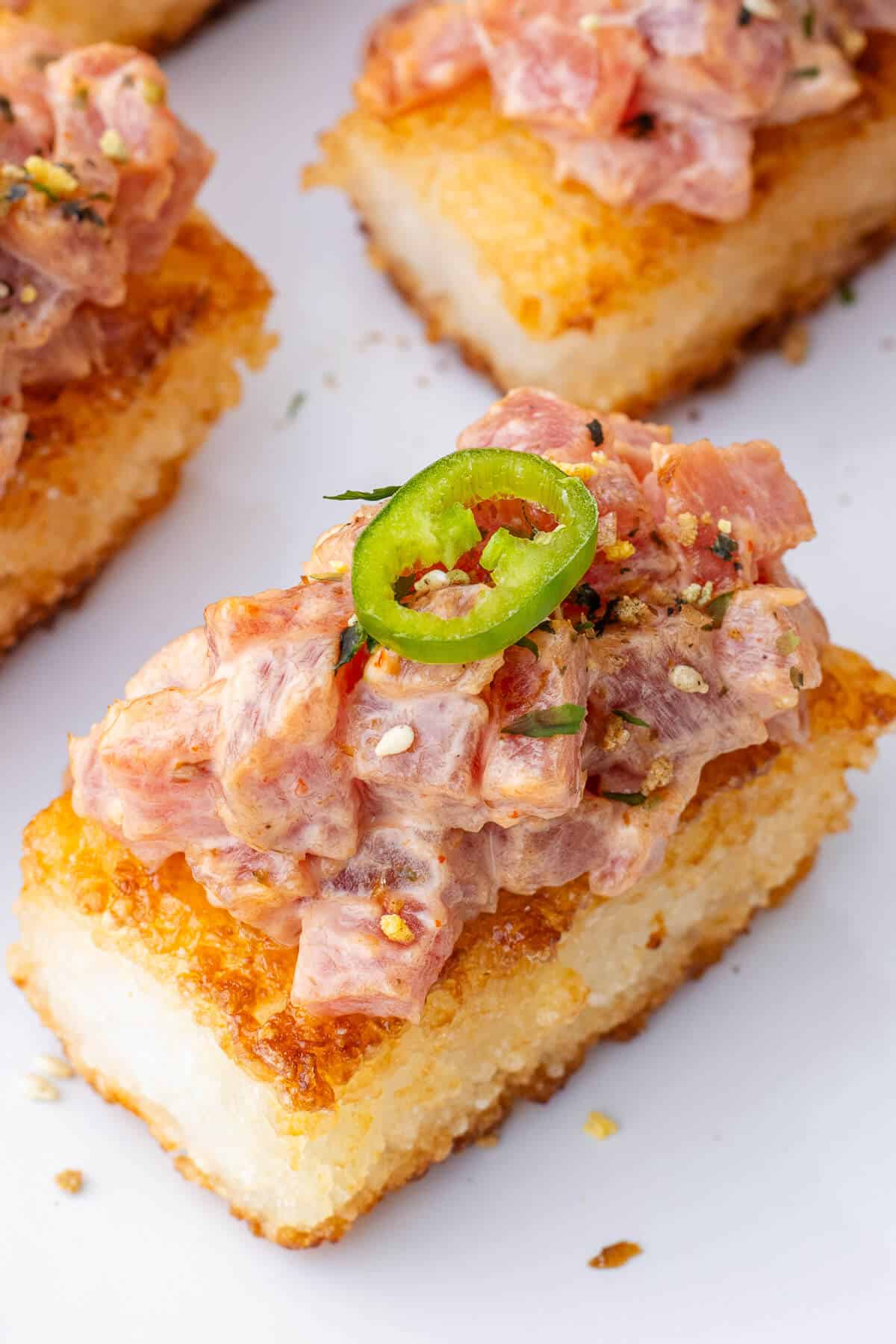 Spicy Tuna Crispy Rice piece with garnish of furikake and a slice of jalapeño